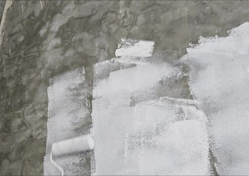 a hand rolling white paint on a smooth dark concrete wall, ideal for home renovation, interior design, DIY repair, wall priming, and construction concepts.