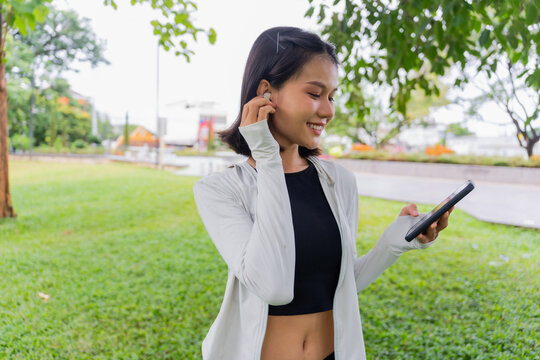 Asian sporty woman using earphone listen to music on smartphone in public park