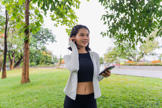 Asian sporty woman using earphone listen to music on smartphone in public park