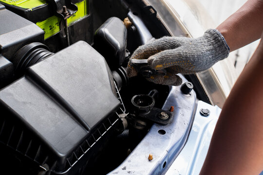 Car mechanic hand wearing protective glove opening radiator cap to inspect engine coolant liquid level.