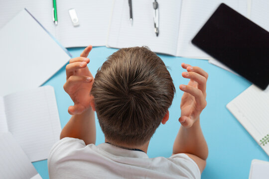 student holding head stressed with homework assignments overwhelmed young boy top view blue background with notebooks and tablet with copy space for banner design, education difficulty psychology
