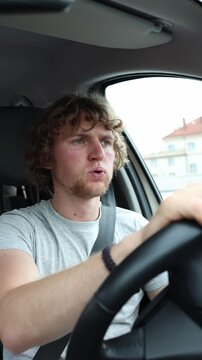 Vertical screen confused driver reacts with visible disbelief behind the wheel while moving through urban traffic appearing puzzled by an unexpected situation on the road