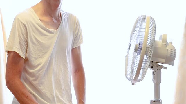 扇風機の風に当たる肌着姿の男性