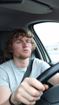 Vertical screen sleepy driver slaps his cheeks to stay awake behind the wheel while the car keeps moving through traffic revealing dangerous fatigue and severe drowsiness