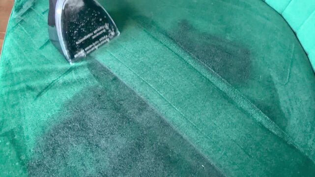 cleaning, satisfying cleaning. A person using a wet vacuum extractor to deep clean the seat cushion of a green velvet sofa.