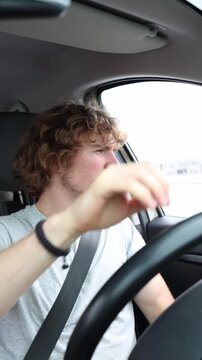 Vertical screen young man becomes extremely nervous and loses his temper behind the wheel after another driver cuts him off during a tense drive through busy city traffic