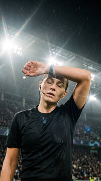 Tired referee wipes forehead under intense stadium lights. Concept of pressure, fatigue and physical demands of sports officiating.