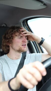Vertical screen nervous driver holds his forehead while traveling through the city showing anxiety tension and mental stress as he tries to stay focused on the road ahead