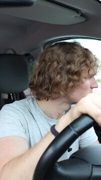 Vertical screen concerned driver listens carefully to strange rattling noises inside the moving car while trying to identify a possible mechanical problem during the trip