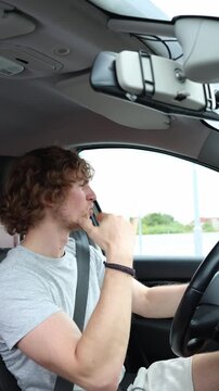 Vertical screen driver dances with one hand to the rhythm while guiding a moving car with the other enjoying music during a city trip and dividing attention from the road