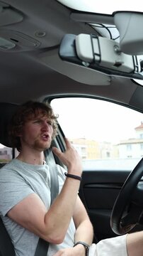 Vertical screen motorist moves his hands and body in a playful dance while driving through the city enjoying favorite music and expressing cheerful energy during the trip
