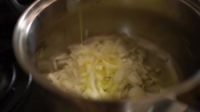 A stream of olive oil pours over onions slowly cooking in a pan, Close-up Shot