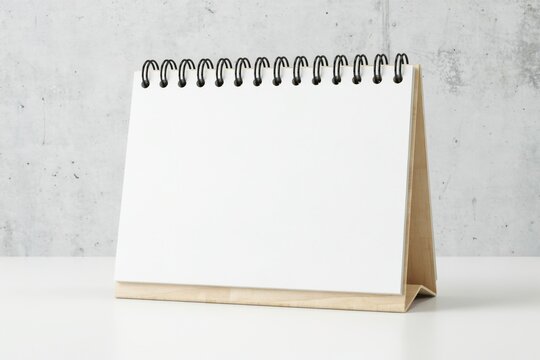 Blank desk calendar mockup on wooden stand against concrete wall