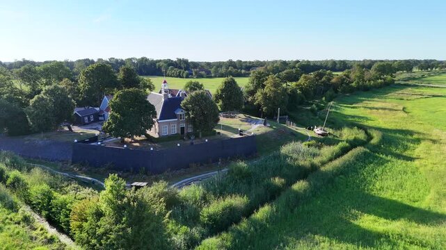 A scenic drone shot capturing the historic former island of Schokland in the Netherlands on a bright, sunny day. rotating shot of the church, showing the old wall and a boat.