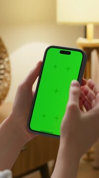 Woman use digital tech cell phone with green screen mock up. Hand tap press phone web site, open app. Girl hold mobile closeup. Turn on page. Cozy home background. Click online game copy space.