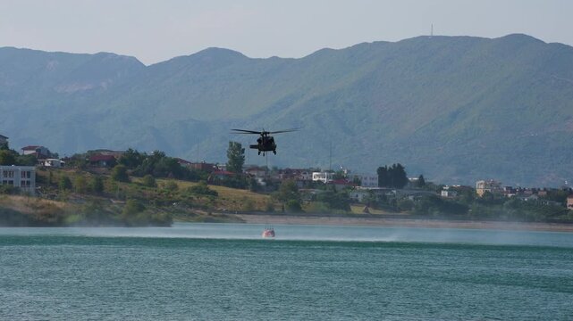 Chopper lowering heavy water bucket via cable into tranquil lake during fire emergency