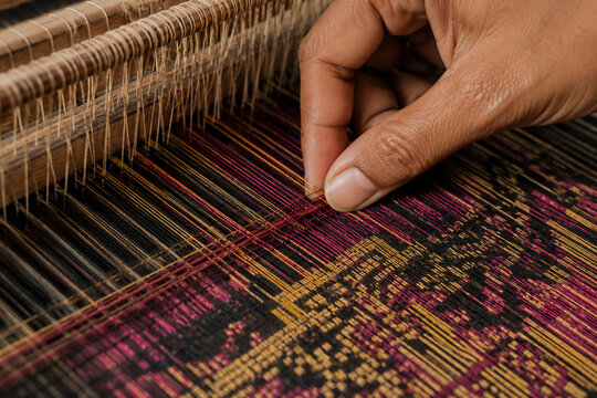 close up of female hands weaving traditional textile on wooden loom