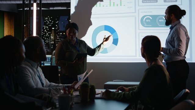 Multiethnic team of workers discuss the financial situation of the company, presenting data forecasts and diagrams to advisory board.