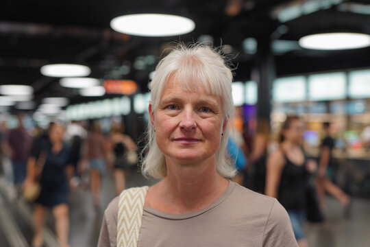Happy senior woman looking and smiling on camera at busy train station in the city - Lifestyle, elderly person and travel concept