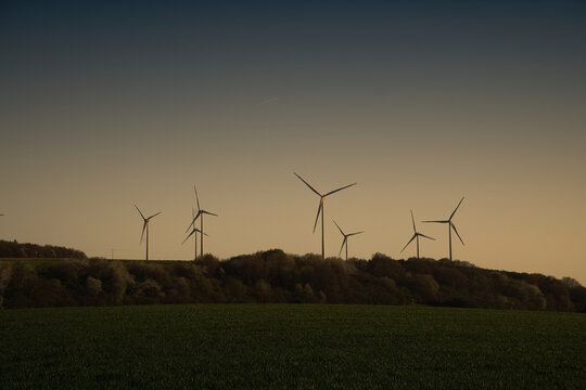 Wind turbines as silhouettes on a hill at twilight.