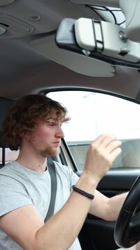 Vertical screen sleepy driver struggles to stay awake behind the wheel and rubs his face while the car is moving trying to fight drowsiness and maintain focus on the road
