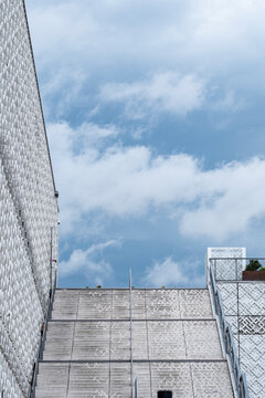 Minimal architecture exterior with concrete walls framing an open sky view where clouds rise above a geometric rooftop detail and textured surfaces
