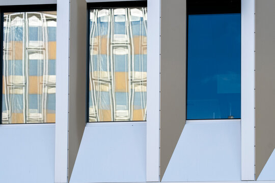 Modern facade with blue windows and glass reflection set into white architecture where vertical geometry defines a clean exterior building detail