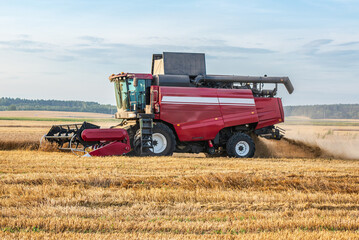 Obraz premium Red combine harvester harvesting wheat on agricultural field