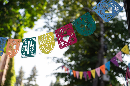 Vibrant festive Papel Picado garland with traditional cut-out patterns against a beautiful blurred bokeh background, design template for Day of the Dead celebration