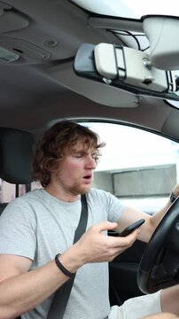 Vertical screen distracted driver looks up from his smartphone in shock when a pedestrian suddenly runs in front of the moving car creating an immediate risk of collision
