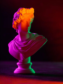 Classical sculpture bust illuminated with vibrant neon lighting on dark background