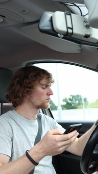 Vertical screen distracted driver stares at a smartphone while driving through the city taking his attention away from the road and creating a serious traffic safety risk

