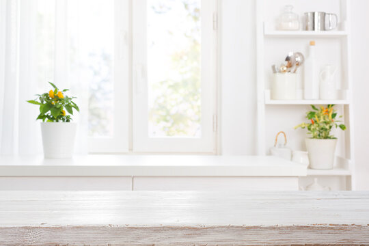 Bleached wooden table top over defocused kitchen curtained window sill and shelf background