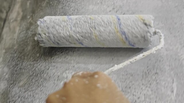 a paint roller applying a fresh coat of white primer onto a raw concrete wall, highlighting tactile surface texture and wet stipple details for home renovation, interior design, DIY repair
