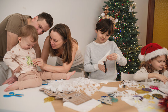 Happy family cut paper snowflakes near Christmas tree, celebrating Christmas with together. New Year's preparations and decorations. Paper crafts. 