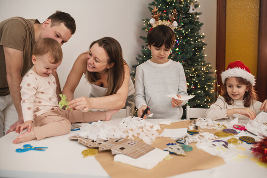 Happy family cut paper snowflakes near Christmas tree, celebrating Christmas with together. New Year's preparations and decorations. Paper crafts. 