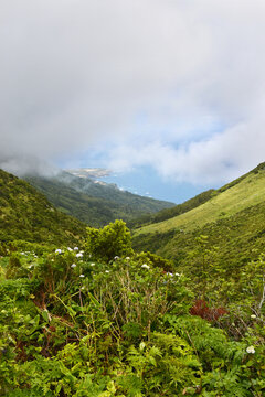View from green hills to coast, glimpse through clouds of Ponta Delgada village and ocean