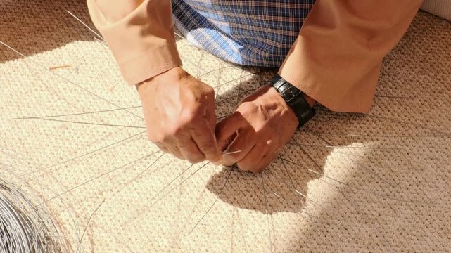 elderly man hands bend and twist metal wire creating fish trap structure. ghazl al gargour shows authentic arabic craft. ghazl al gargour passes mastery down through generations.