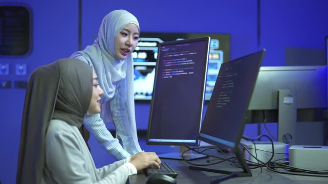 Two Muslim women programmers in hijab collaborating on software code in a modern tech office.