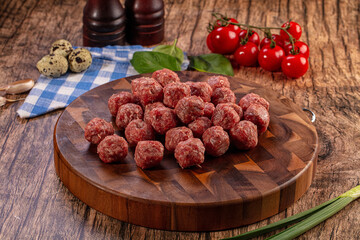 Raw meatballs on a wooden cutting board with fresh ingredients