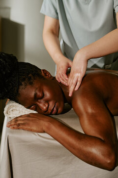 Vertical image of young adult African American woman receiving professional back massage at wellness spa. Image suitable for beauty salon marketing and healthcare advertising