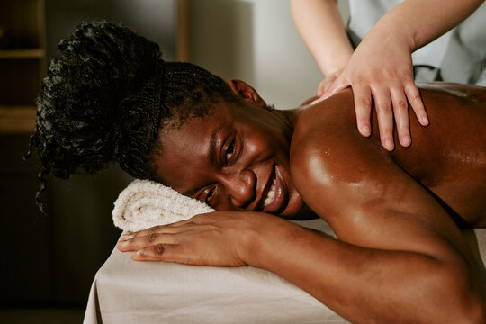 Portrait of smiling young adult African American woman receiving back massage from therapist in wellness spa. Image is suitable for beauty salon marketing and self care promotions