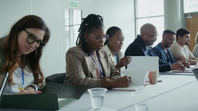 Diverse group of professionals focused, taking notes and engaging in a corporate business meeting. This represents collaboration and learning in a professional environment.
