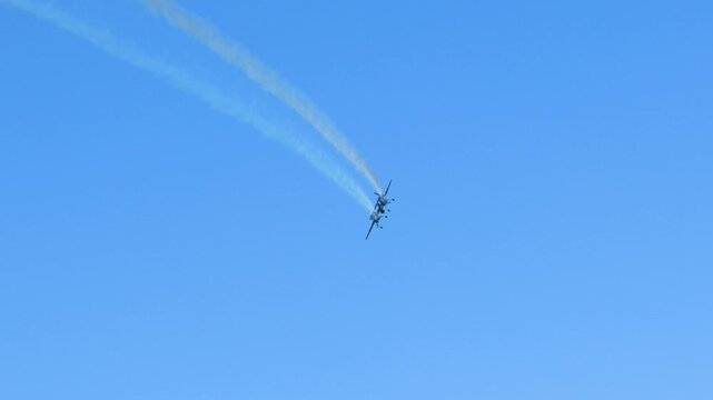 Stunt Biplane Performing Aerobatics with Smoke Trails in Clear Blue Sky