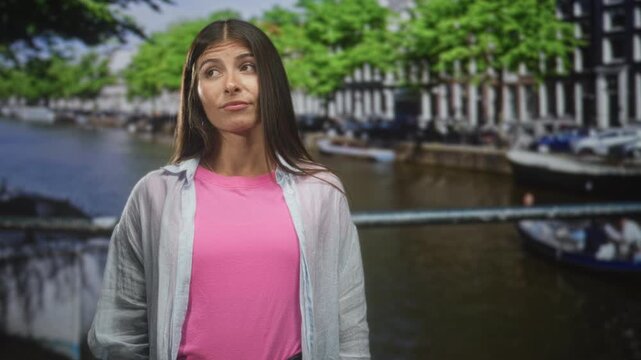 Woman pointing finger toward camera wearing pink tshirt by canal on a street; confidence assertiveness.