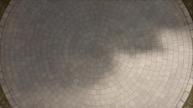 Circular Stone Tile Pattern Cinematic City Timelapse Background with Radial Symmetry, Geometric Mosaic Texture, Weathered Pavement, Dramatic Natural Light, and Architectural Design Detail