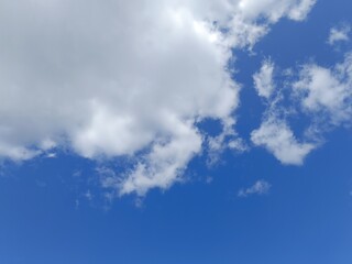 Fototapeta premium Fluffy white cumulus clouds against a bright blue sky. Sunny summer daytime weather background