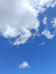 Fototapeta premium Vertical photo of a bright blue sky with fluffy white cumulus clouds. Sunny daytime weather background with a small isolated cloud