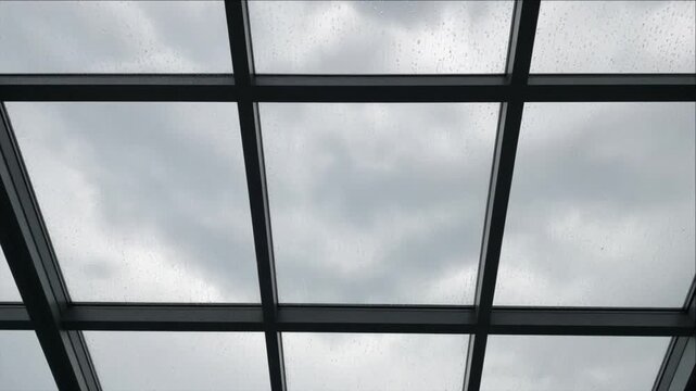 Cinematic City Timelapse Background Through Rain Covered Glass Roof Skylight with Dark Geometric Metal Frame Grid and Moody Cloudy Architecture Atmosphere for Urban Travel Visuals