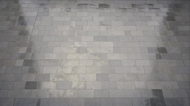 Cinematic city timelapse background featuring gray stone pavement surface with rectangular tiled pattern, subtle light variation, monochrome geometric texture, and soft industrial urban texture